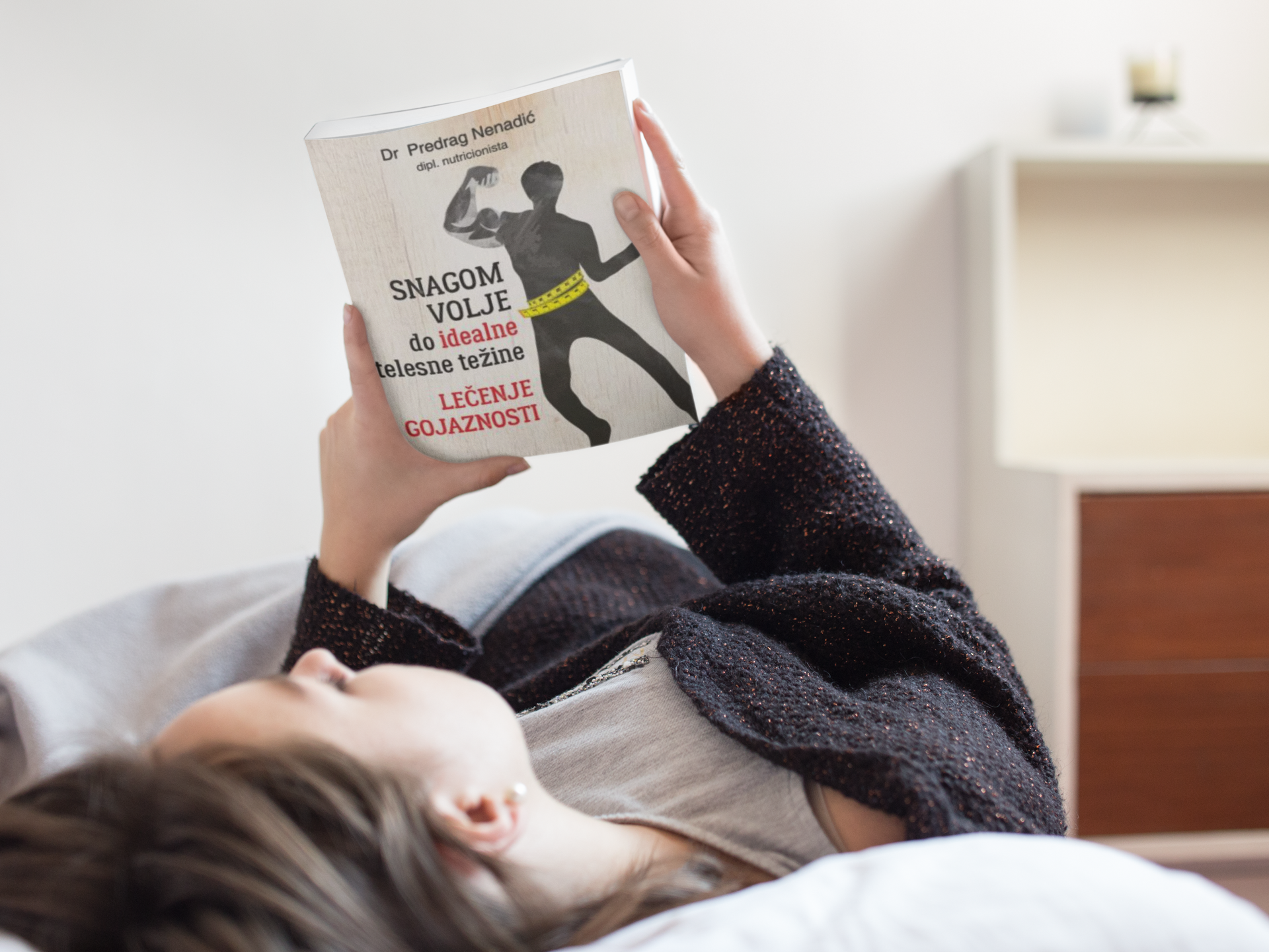 young-girl-looking-at-a-book-cover-while-lying-down-in-her-bed-mockup-a14302